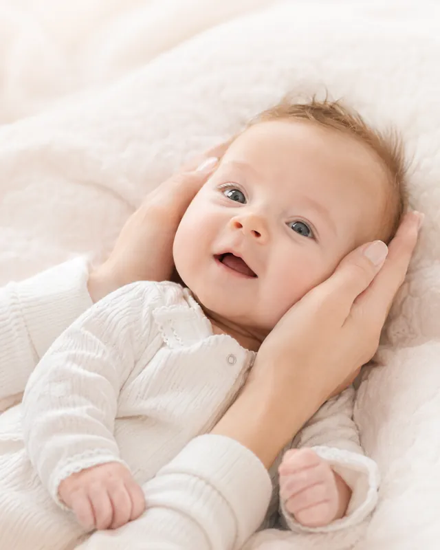 A smiling baby cradled gently in a parent's hands
